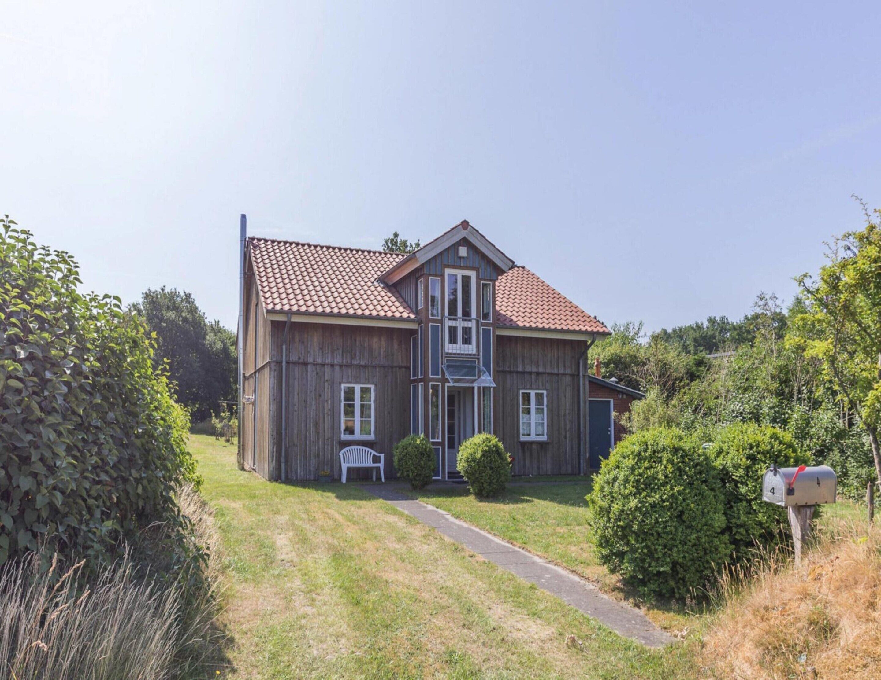 A two-story wooden house with a red-tiled roof, a front porch, and a mailbox.