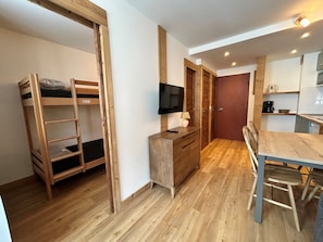 Quarto compacto com cama beliche, escrivaninha com TV, mesa de jantar e cozinha compacta.