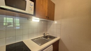 A kitchen with white tiles, a microwave, a stove, a sink, and wooden cabinets.