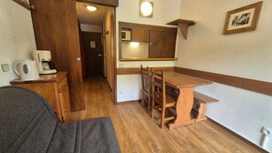 A compact kitchen with wooden cabinetry, a dining table, and chairs. A coffee maker and kettle are on the counter.