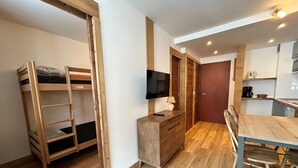 Une chambre compacte comprenant un lit superposé, un bureau avec télévision, une table à manger et un coin cuisine.