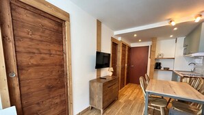 Una cocina compacta con armarios de madera, una mesa de comedor con sillas, un televisor sobre un mueble de madera y una puerta roja.
