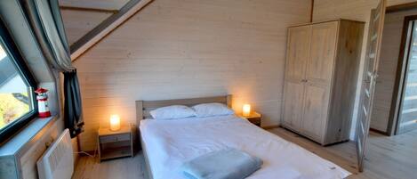 A bedroom with a wooden bed, bedside lamps, a wardrobe, and a window with curtains.