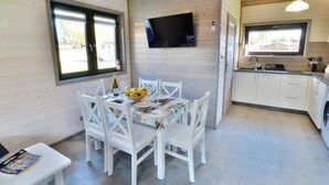 A modern kitchen with white cabinetry, a dining area with a table set for four, and a TV mounted on the wall. - Comfortable Holiday Homes With air Conditioning (Ustronie Morskie)