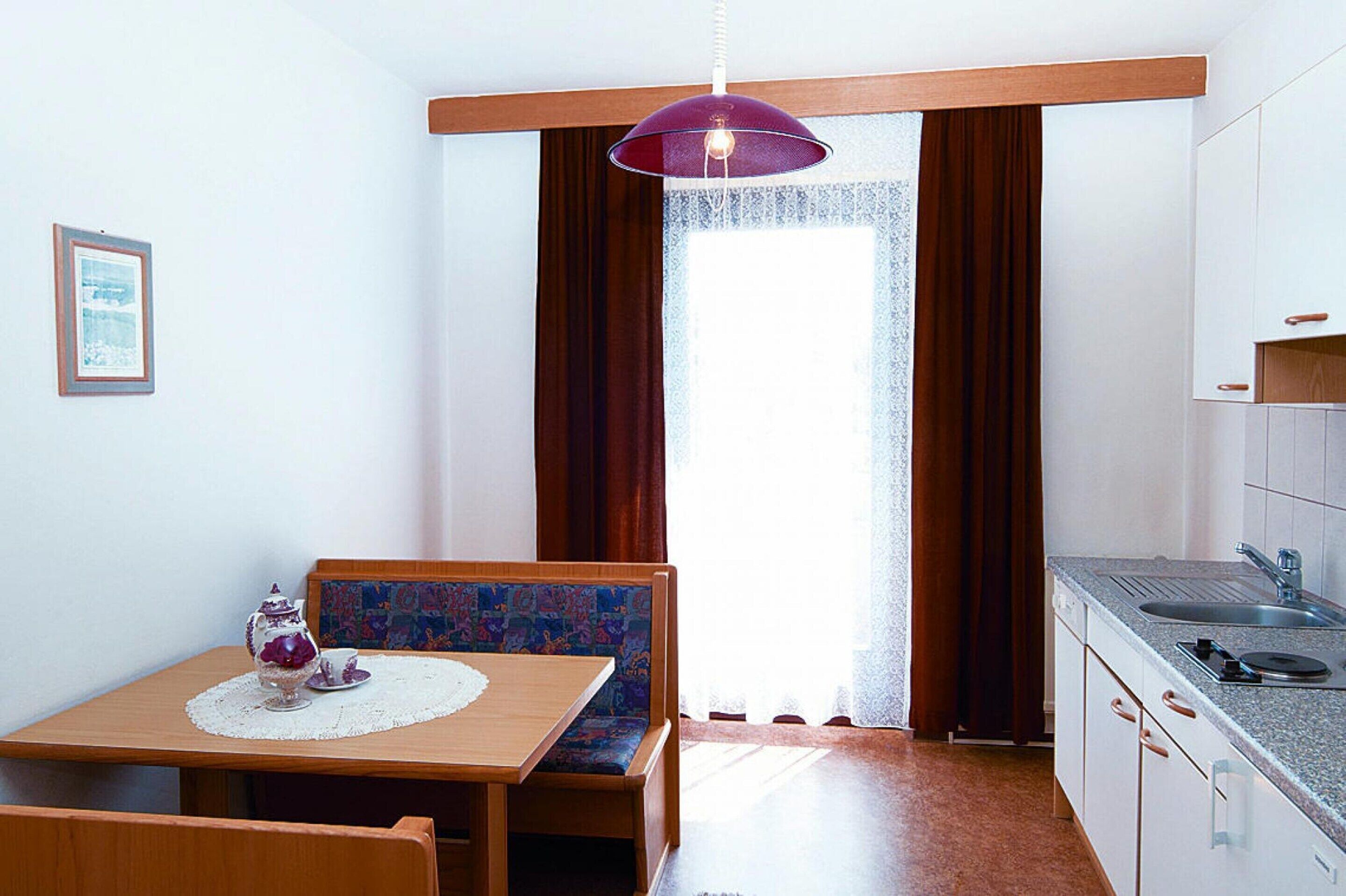 Una cucina compatta con zona pranzo, una finestra con tende e una lampada a sospensione.