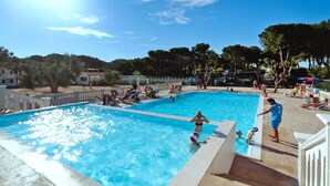 A swimming pool area with multiple pools, surrounded by a white fence, and people engaging in various activities. - Bungalow in a Resort in Lido del Sole With Terrace (Rodi Garganico)