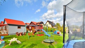 Un parque infantil con columpios, toboganes y un trampolín, rodeado de casas con techos rojos.