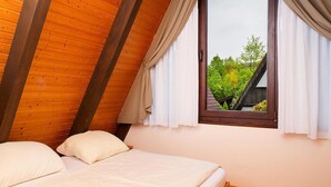 Een slaapkamer met een houten plafond, een enkel bed en een raam met gordijnen.