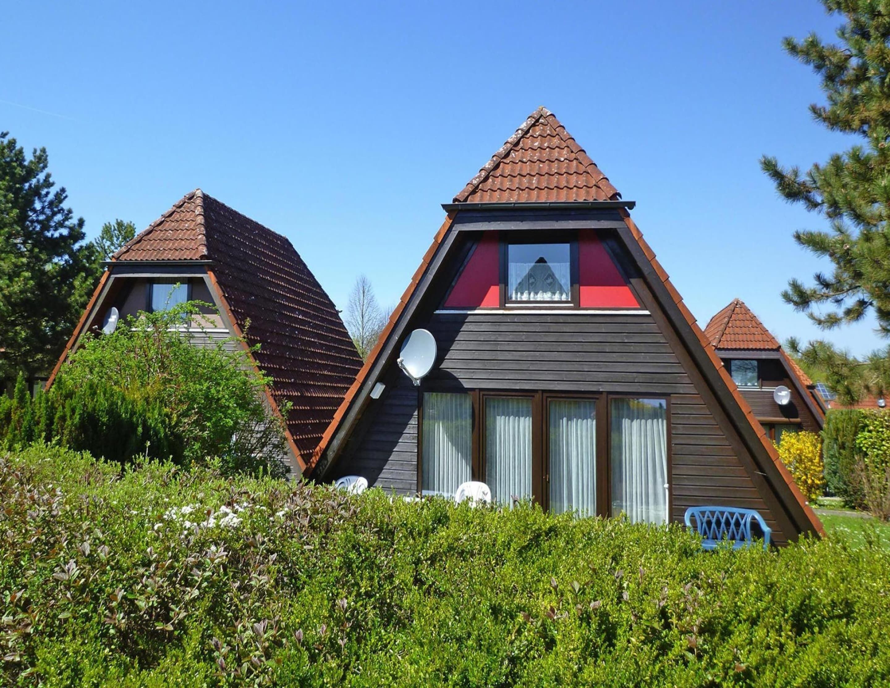 A modern, triangular-shaped house with a sloped roof, large windows, and a satellite dish.