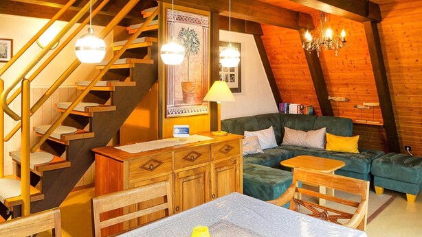 Een gezellige kamer met een houten trap, een zithoek, een eettafel en een kroonluchter.