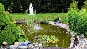 Un jardin avec un étang, une statue et une terrasse en bois.