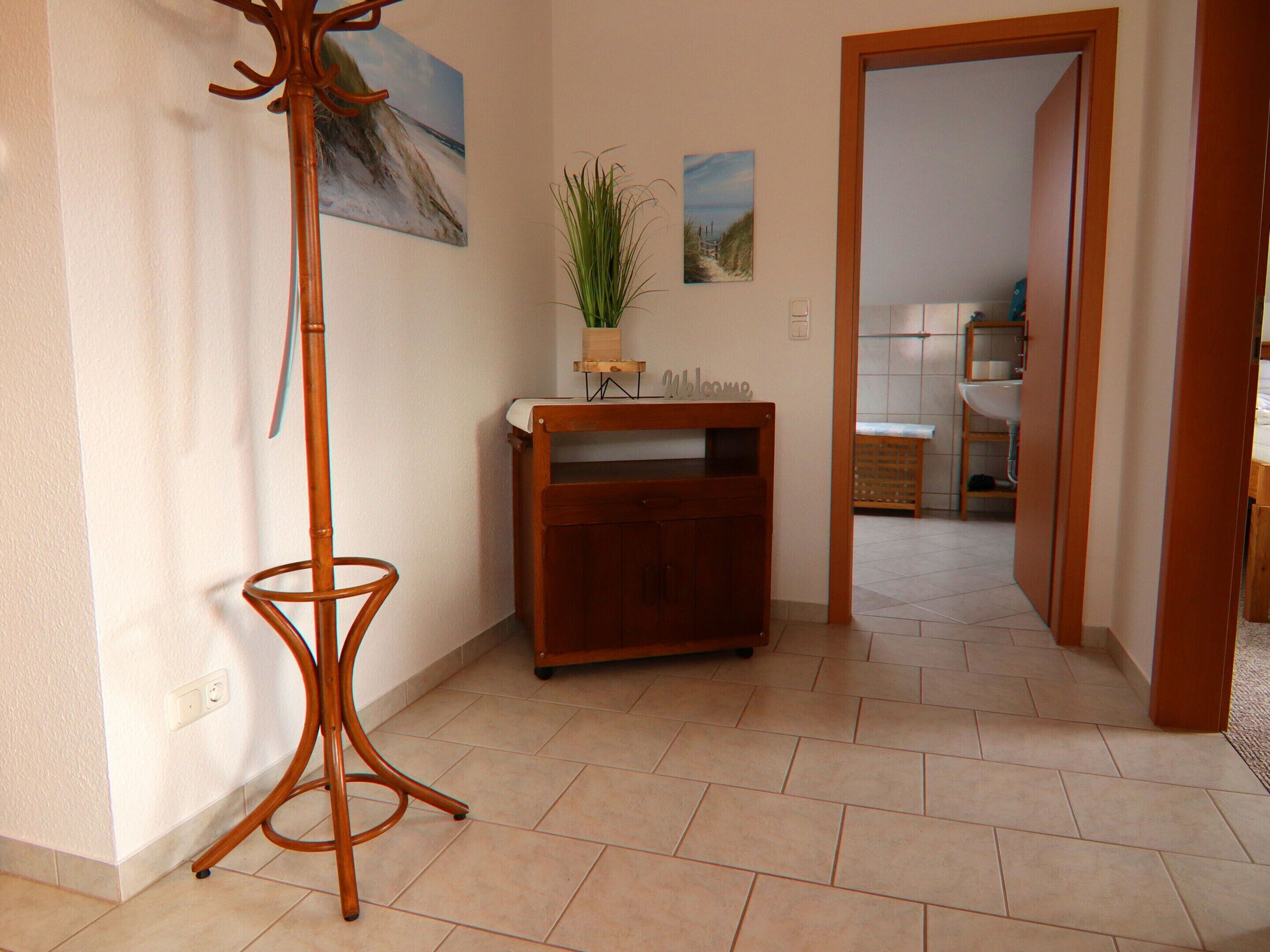A hallway with a wooden floor, a coat stand, a small wooden cabinet, and two wall-mounted paintings.