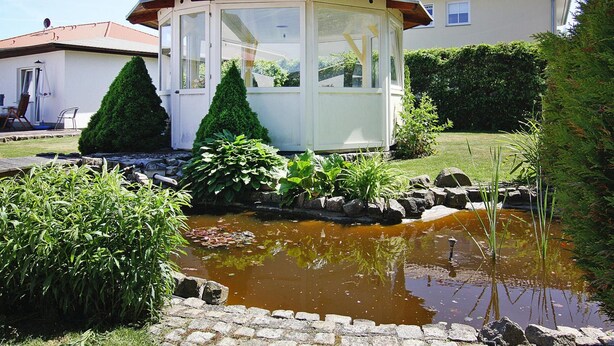 Une maison avec une véranda, un étang et un jardin.