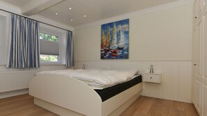 A bedroom with a bed, a window with curtains, a painting on the wall, and a nightstand. - Ferienwohnung in Wyk Boldixum for Vier Personen (Wyk auf Foehr)
