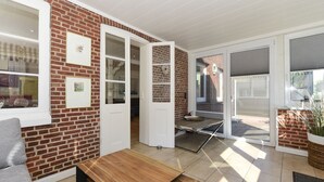 A spacious living area with a brick wall, a sliding glass door leading to an outdoor space, and a wooden coffee table. - Ferienwohnung in Wyk Boldixum for Vier Personen (Wyk auf Foehr)
