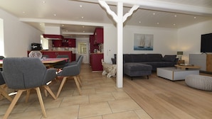 A modern living room with a grey sofa, a dining area with grey chairs, and a kitchen in the background. - Ferienwohnung in Wyk Boldixum for Vier Personen (Wyk auf Foehr)