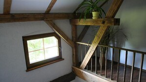 Ein Zimmer mit schrägem Dach, einem fensterartigen Gitter und einer Holztreppe mit Geländer.