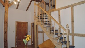 Eine Holztreppe mit blauen Stufen und ein Holzstuhl in einem Raum mit weißen Wänden und einer Holztür.