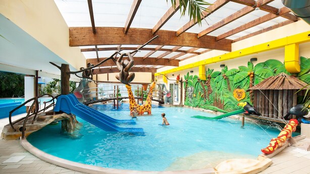 Ein Hallenbad mit Rutschen, einer Kletterlandschaft und einer Wandmalerei von tropischem Grün.