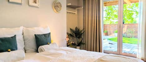A bedroom with a large bed, a wall clock, and a sliding glass door to a garden.