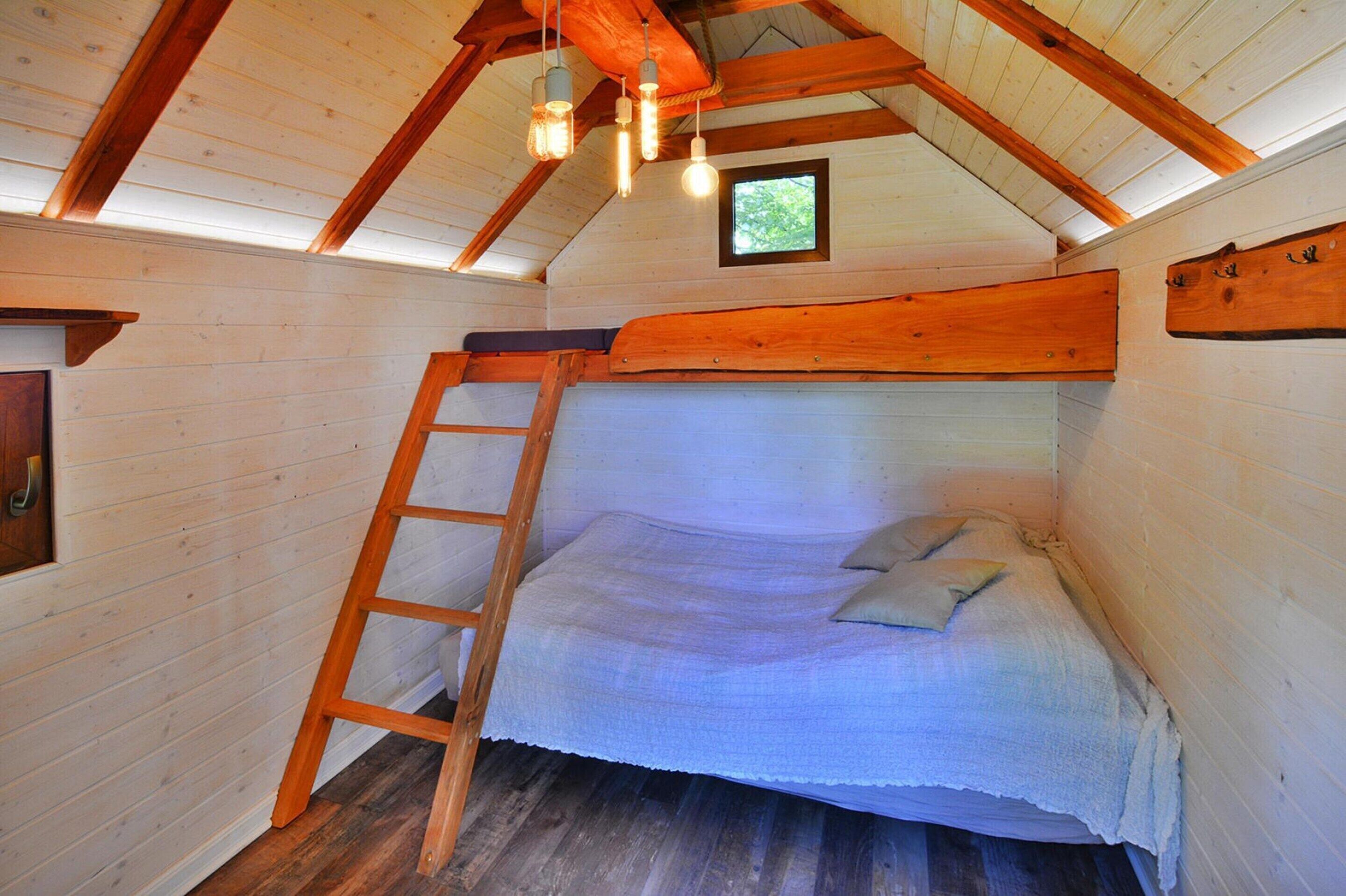 Une petite chambre mansardée, chaleureuse et accueillante, avec un lit superposé, une échelle en bois et une petite fenêtre.