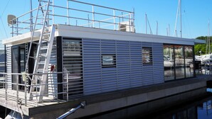 A modern floating house with a metal exterior, large windows, and a visible deck area. - Hausboot in Boltenhagen (Boltenhagen)