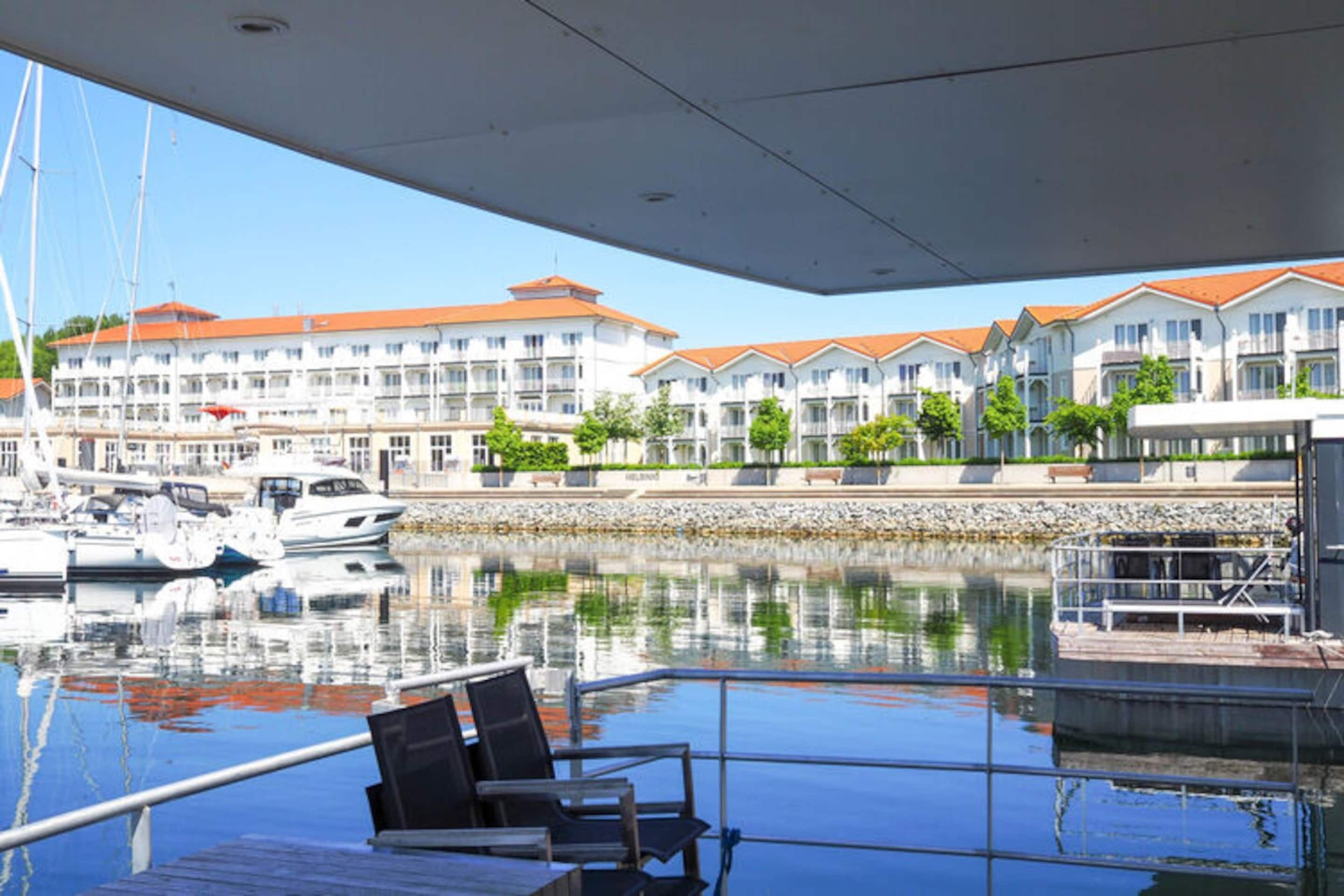 A marina with boats docked, a covered area with seating, and a building with balconies in the background.