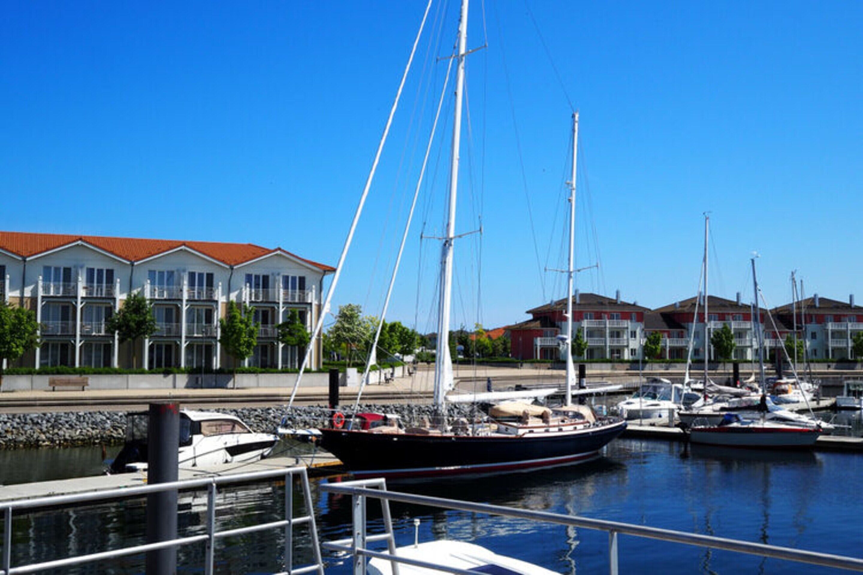 A marina with several boats docked, a building with a red roof, and a clear blue sky.