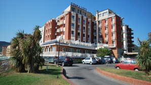 A multi-story hotel with balconies, a parking lot, and a clear sky. - Pietra Ligure Beach Residence for 4 (Pietra Ligure)