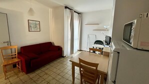 A compact living space with a red sofa, a dining table with chairs, a small kitchen area with a microwave, and a single chair. - Pietra Ligure Beach Residence for 4 (Pietra Ligure)