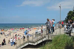 Ein Strand mit Menschen auf einer Betonstiege mit Blick auf Sand und Meer.
