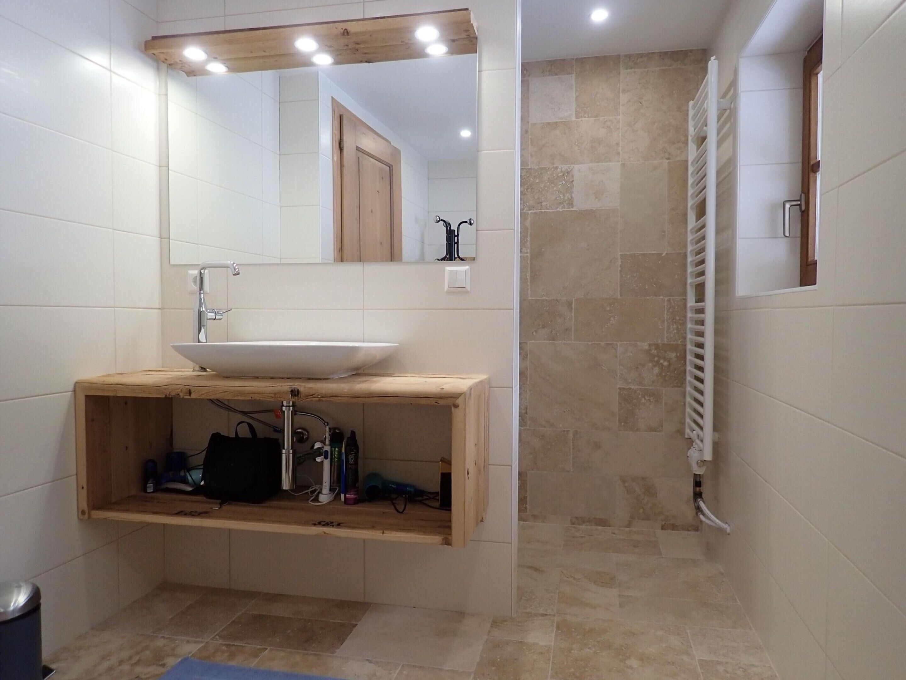 Ein modernes Badezimmer mit einem Holzkosmetikschrank, einem großen Spiegel und einer Duschkabine.