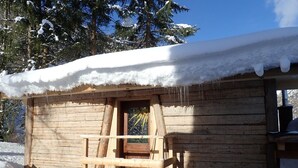 Une cabane en bois, dont le toit est recouvert de neige, et qui possède un porche en bois.