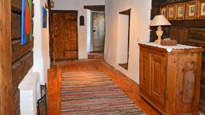 Un couloir en bois orné d’un tapis coloré à motifs tissés, d’une armoire en bois surmontée d’une lampe, et de tableaux encadrés accrochés au mur.