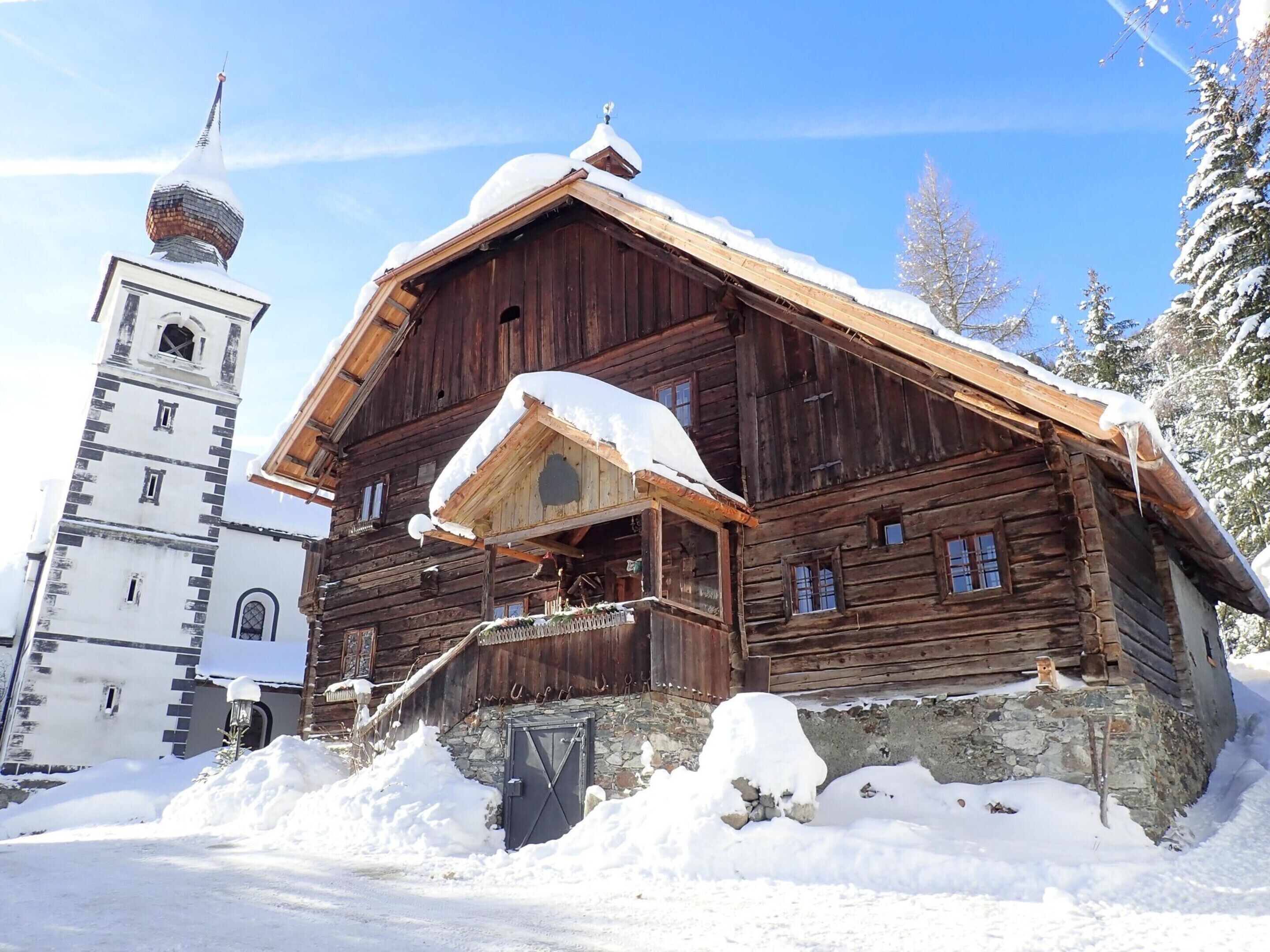 A wooden log cabin with a steeply pitched roof and a bell tower, surrounded by snow.