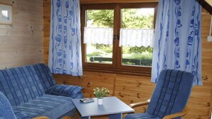 A cozy cabin room with a sofa, two armchairs, a small table, and a window with curtains. - Two-story Holiday Homes With Terraces (Mielno)