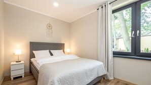 A neatly arranged bedroom with a bed, bedside tables, and a window with curtains. - Comfortable Apartments Close to the Beach Darlowko (Darlowo)