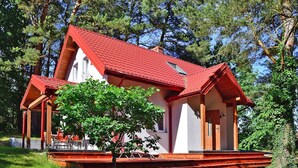 Una casa a due piani con tetto rosso e pareti bianche, immersa nel verde.