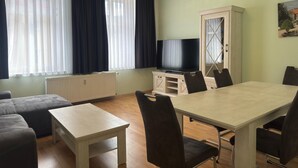 A furnished living room with a sofa, a dining table, chairs, a TV, and a cabinet. - Ferienwohnung Otto der Reiche in Ballenstedt (Ballenstedt)