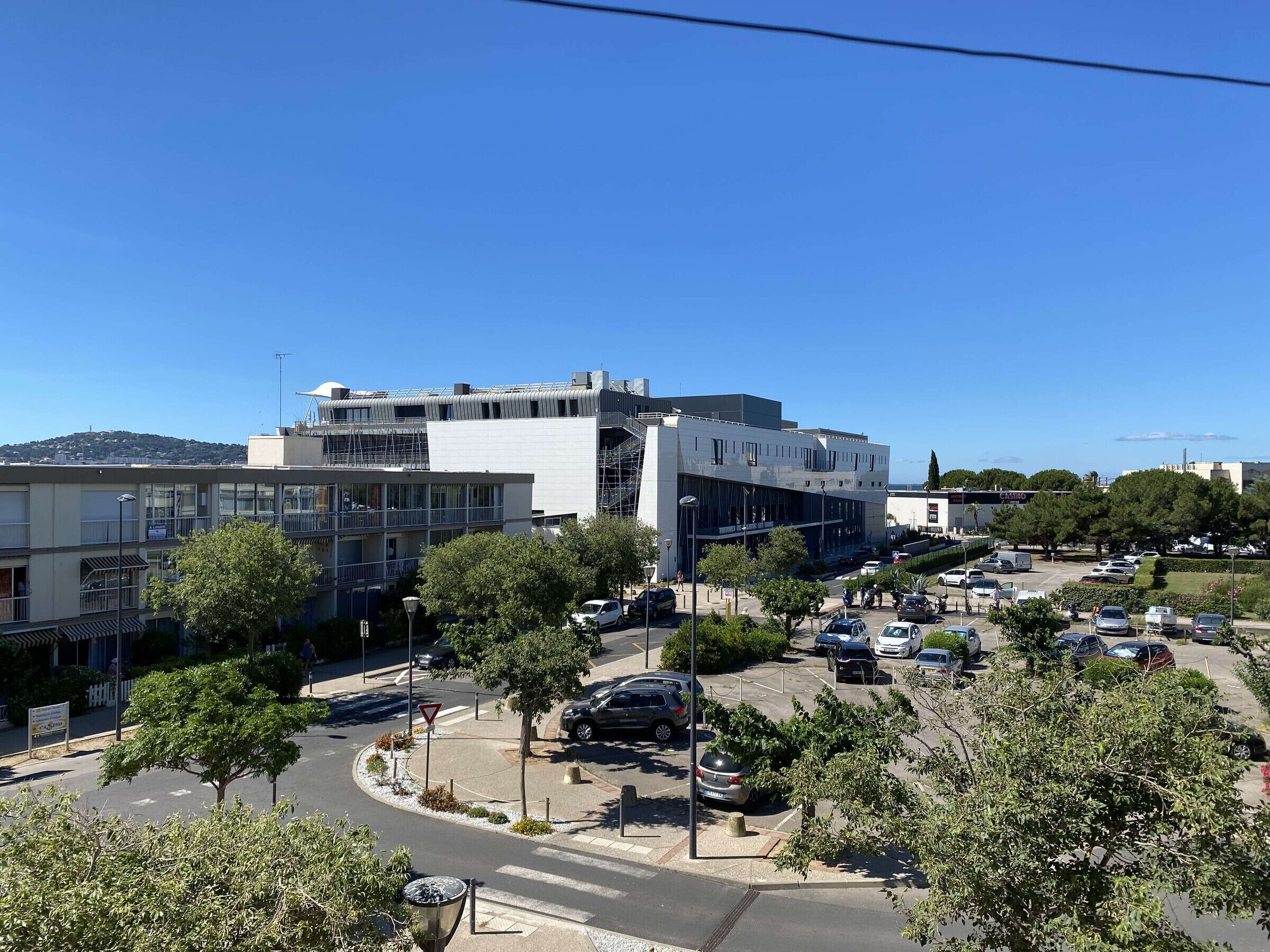 A modern building with multiple floors, surrounded by a parking lot and trees.