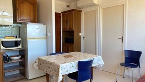 Una cocina compacta con refrigerador, microondas y armarios de madera. En el centro, una mesa de comedor con sillas.