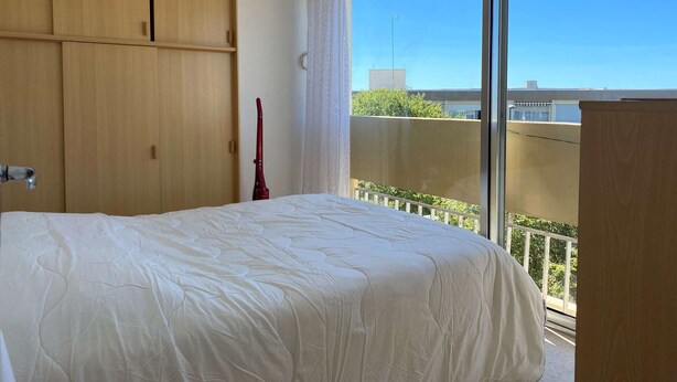 Un dormitorio con cama, armario de madera y un ventanal con vistas a zonas verdes y edificios.
