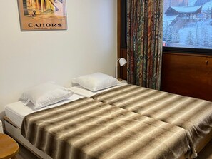 Een hotelkamer met twee bedden, een raam met gordijnen, een poster aan de muur en uitzicht op een besneeerd landschap.