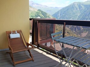Een balkon met een houten stoel en tafel, met uitzicht op een bergachtig landschap.