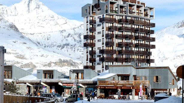 Un hotel a più piani con balconi, un ristorante e vista sulle montagne innevate.
