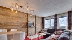 Un accogliente soggiorno con una parete in legno, un tappeto rosso, un divano, una TV e un'area pranzo con sedie e un tavolo.