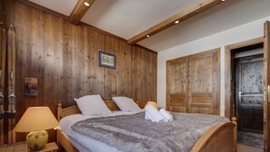 A wooden-paneled bedroom with a large bed, a nightstand, and a door. - Spacious Apartment 6 People · Balcony · Wifi in Tignes Le Lac (Tignes)