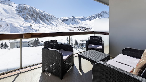 A balcony with wicker furniture, a clear view of snow-covered mountains, and a cityscape in the background. - Spacious Apartment 6 People · Balcony · Wifi in Tignes Le Lac (Tignes)