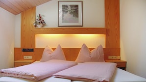 Une chambre d’hôtel avec un lit, une tête de lit en bois, des tables de chevet, une petite table, une horloge murale et un tableau encadré au-dessus de la tête de lit.