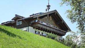 Un chalet traditionnel avec un toit Ă forte pente, des balcons en bois et un girouette au sommet.